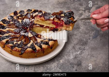La mano della donna tiene la lama della spalla con un pezzo di crostata di prugna o torta, primo piano, messa a fuoco selettiva Foto Stock