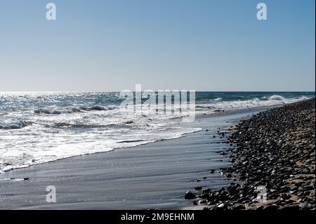 mare con una spiaggia di pietra e calme onde sotto un cielo blu Foto Stock