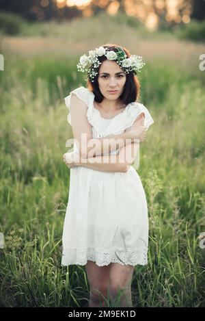 Bella ragazza brunetta caucasica in abito bianco e con corona in posa campo estivo Foto Stock