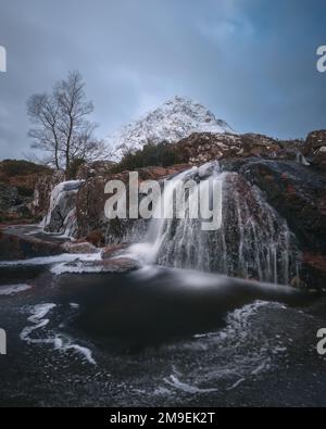 Fiume di montagna e cascata parzialmente ghiacciata ai piedi del Buachaille coperto di neve Etive Mor. Cascata di Etive Mor. All'ingresso della valle di Glencoe nelle Highlands scozzesi, Scozia Foto Stock