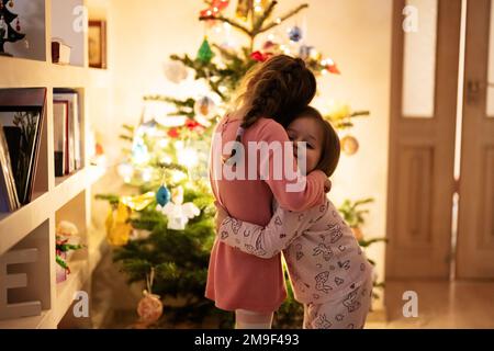 Due sorelle insieme vicino all'albero di Natale a casa di sera. Foto Stock