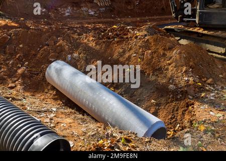 Lavoratore che posa tubi di liquame in terra, preparando mettere tubi di calcestruzzo sotterraneo Foto Stock