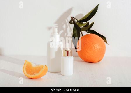 Flaconi di siero cosmetico e frutti d'arancia su sfondo bianco. Concetto naturale di cosmetica, mockup. Foto Stock