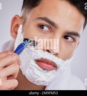 Un buon rasoio aiuta a prevenire tagli e tagli. un giovane uomo che rasa la barba sullo sfondo di uno studio. Foto Stock