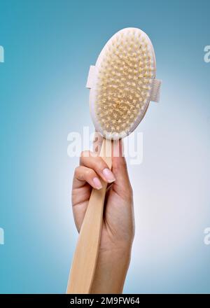 Il suo giorno esfoliato. una donna irriconoscibile che tiene una spazzola per il corpo su uno sfondo blu in studio. Foto Stock