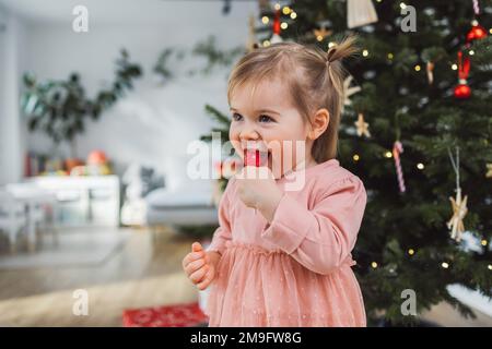 La bambina sorridente ama leccarle il suo lecca lecca lecca il giorno di Natale Foto Stock