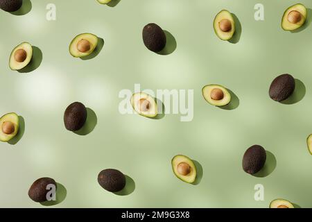 Vista dall'alto di avocado fresco maturo dimezzato e sano posto su una superficie verde pallido alla luce del sole come sfondo astratto Foto Stock
