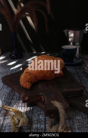 Croissant su un vassoio di legno con un vaso di fiori e una tazza di tè sullo sfondo Foto Stock
