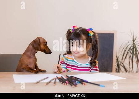 carino ragazza piccola disegna con il suo cane amico dachshund. Bambini e animali. Cani ammessi Foto Stock