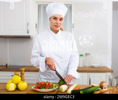 Donna proffesional cuoca in bianco uniforme tagliando verdure Foto Stock