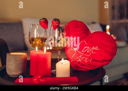 Festa di San Valentino a casa con bicchieri da vino champagne con fragole in cima circondato da candele Foto Stock