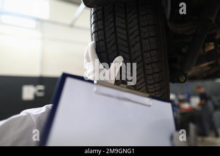 Il tecnico meccanico dell'auto tiene in mano un foglio di appunti vuoto con testo dello spazio di copia e pneumatici per auto Foto Stock