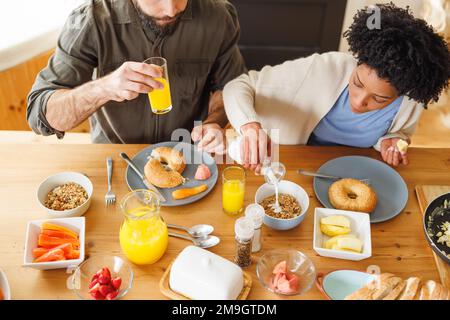 Vista dall'alto della giovane coppia biraciale che serve la colazione insieme sul tavolo da pranzo a casa Foto Stock