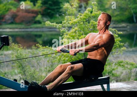 Uomo che si esercita sulla macchina di canottaggio all'aperto, Bainbridge Island, Washington, USA Foto Stock