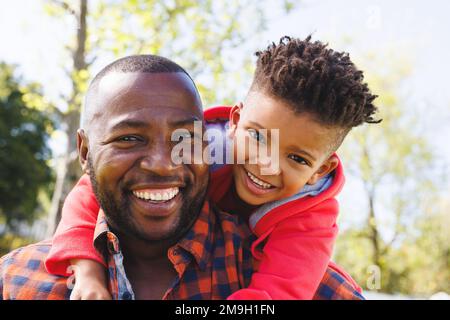 Ritratto di felice padre e figlio afroamericano che abbraccia e sorride nel loro cortile Foto Stock