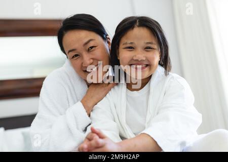 Ritratto di felice madre asiatica e figlia seduta a letto Foto Stock