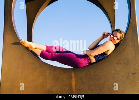 Donna in occhiali da sole sdraiata su una struttura circolare e guardando la macchina fotografica, Seattle, Washington state, USA Foto Stock