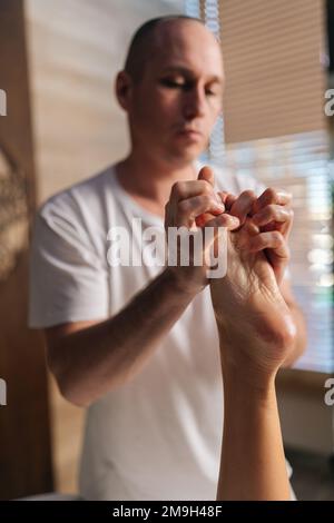 Primo piano ripresa verticale di un medico ortopedico maschile che fa il massaggio del piede e della gamba inferiore di una paziente femminile non riconoscibile dopo la lesione caviglia radente dentro Foto Stock