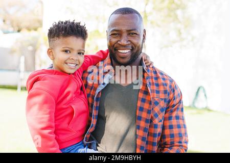 Ritratto di felice padre e figlio afroamericano che abbraccia e sorride nel loro cortile Foto Stock