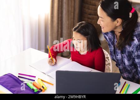 Felice asiatica madre e figlia seduto a tavola e facendo i compiti a casa Foto Stock