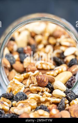 Vaso di vetro pieno di noci assortite con mandorle, nocciole, anacardi e uvetta, in una macro foto ripresa. Foto Stock