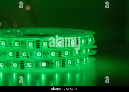 Rotolo di striscia a LED a inseguimento con lampade verdi al neon luminose poste sul tavolo in una stanza buia Foto Stock