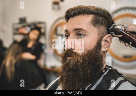 Hippster uomo al salone barbershop ottenere barba e capelli taglio -  parrucchiere donna con rasoio elettrico per la rifinitura della barba -  Barbiere concetto negozio Foto stock - Alamy