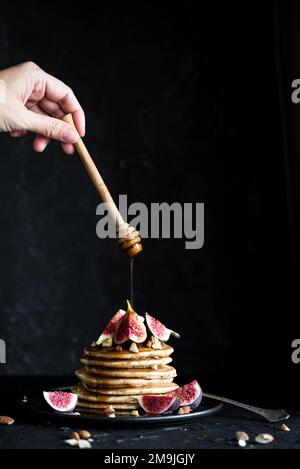 Pila di pancake con fichi, noci e miele scorrevole. Fatto in casa. Sfondo scuro. Frittelle di latticini soffici con fichi e sciroppo versando sopra. Delizioso Foto Stock