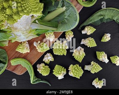 Vista dall'alto di fiori crudi romanesco broccoli appena tagliati su piatto di ardesia nera, preparazione di cavolfiore romano Foto Stock