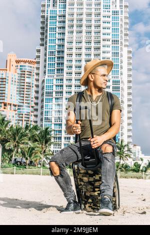 Giovane uomo che arriva al resort sulla spiaggia, indossando un cappello da cowboy, una t-shirt, jeans e scarpe chiuse. Foto Stock