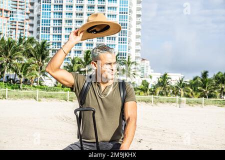 Primo piano di un bel giovane che togli il cappello. Eleganti edifici alberghieri sullo sfondo. Concetto di viaggio Foto Stock