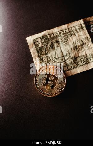 Un colpo verticale di un Bitcoin giacente su un disegno di legge di un dollaro sbriciolato su uno sfondo a gradiente nero Foto Stock