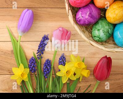 Collezione di colorati fiori primaverili con uova di pasqua in cesto su sfondo di legno, vista dall'alto dei primi fiori nel periodo pasquale Foto Stock