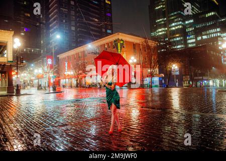 Donna in cappello di Santa con ombrello su strada, Seattle, Washington, USA Foto Stock