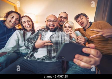 Gli amici a casa prendono selfie, ridendo, avendo buon tempo. USA il telefono per videochiamare in remoto e scattare foto con selfie diversity. Foto Stock