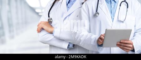 Medici irriconoscibili che si pongono in ospedale, tenendo un tablet digitale Foto Stock