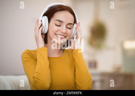 Felice giovane donna che usa le cuffie wireless a casa Foto Stock