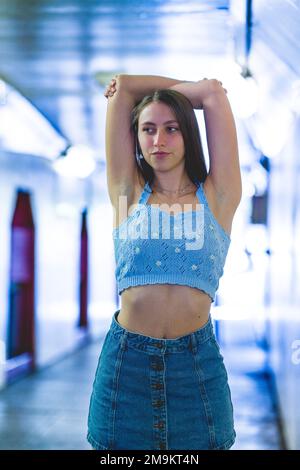 Ritratto a metà corpo di una ragazza teenage alla moda in denim blu e maglia con le braccia sopra la testa in un tunnel Foto Stock