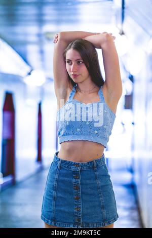 Ritratto a metà corpo di una ragazza teenage alla moda in denim blu e maglia con le braccia sopra la testa in un tunnel Foto Stock