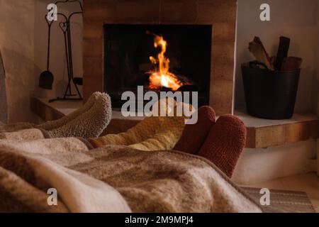 Piedi di persone irriconoscibili con calzini invernali nel calore del camino - concetto inverno, comfort casa Foto Stock