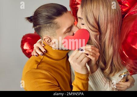 Felice coppia innamorata festeggia San Valentino e bacia dietro una carta rossa di San Valentino Foto Stock