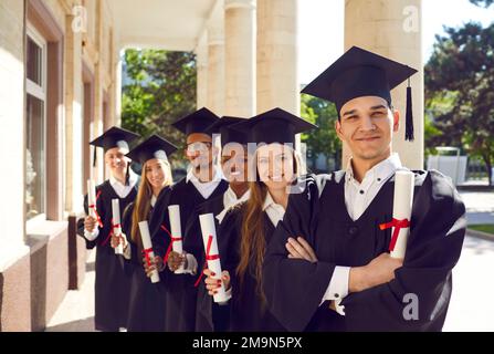 Ritratto di gruppo di laureati felici in berretti e camici con diplomi e sorridenti Foto Stock