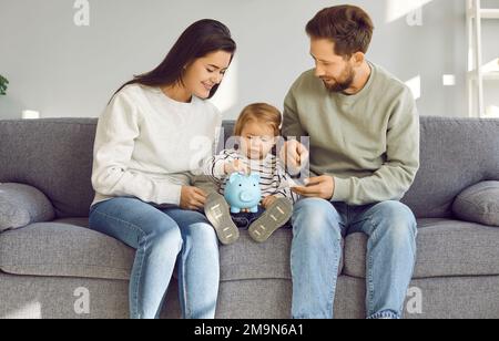 Genitori sorridenti che insegnano al bambino toddler come risparmiare i soldi Foto Stock