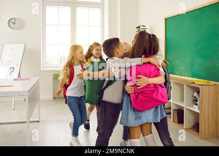 I gioiosi studenti delle scuole elementari si riuniscono in circolo e si abbracciano a scuola prima delle lezioni. Foto Stock