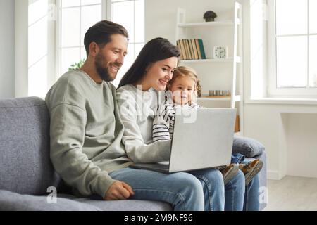 Famiglia felice di mamma, papà e bambina simpatica seduta a casa sul notebook Foto Stock