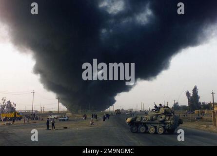 Il fumo proveniente da un giacimento di petrolio in fiamme sale nell'aria mentre i Marines del corpo Marino degli Stati Uniti (USMC) assegnati a D/ Company, 1st Battaglione di rinascita blindato, 1st Divisione Marina, guidano il loro veicolo blindato di luce (LAV-25) verso Baghdad, Iraq, durante l'operazione LA LIBERTÀ IRACHENA. Soggetto operativo/Serie: BASE PER LA LIBERTÀ IRACHENA: Baghdad Paese: Iraq (IRQ) Foto Stock