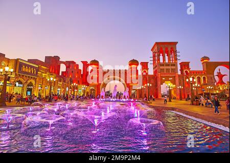 DUBAI, Emirati Arabi Uniti - 6 MARZO 2020: Le fontane danzanti illuminanti in Piazza della Cultura del Global Village Dubai, con una vista sulle torri barjeel (windcatchers) e. Foto Stock