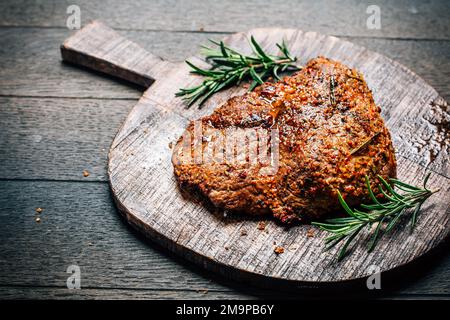Bistecca di manzo alla griglia con spezie sul tagliere su sfondo di legno Foto Stock