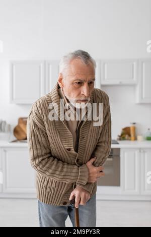 uomo anziano depresso con malattia di parkinson in piedi con la canna da camminata in cucina, immagine di scorta Foto Stock