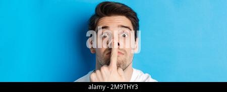 Headshot di un ragazzo caucasico che fa espressioni divertenti, in piedi su sfondo blu Foto Stock